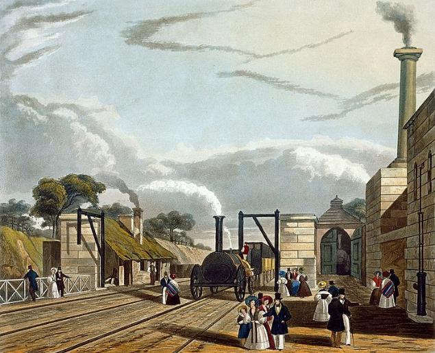 A steam train is stopped at a water-filling station and steam issues from its funnel. People in Victorian dress are standing around; a couple are even on the track in front of the locomotive. To the left is a single storey station station building with a green mossy roof. To the right are more substantial stone buildings with a tall, smoking chimney.