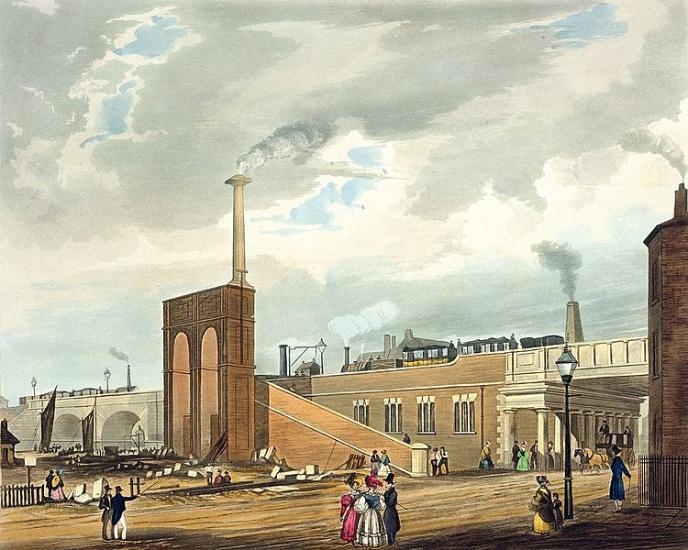 A complex industrial scene showing a street with Victorian figures in colourful dress in the foreground. In the background rise railway buildings. There is a ramp to take goods and people up to a raised railway line and there is a steam train running along the line. To the right is a bridge that goes under the line and to the left is a canal with sailing boats.