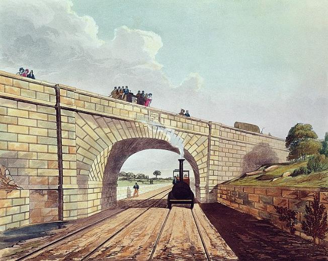 This image has been composed so the viewer seems to be stood on the tracks with a steam locomotive puffing towards them. It is just passing underneath the arch of a bridge which has people looking down, some are sat on a horse-drawn coach. To the right is a stone embankment topped with grass and trees. 