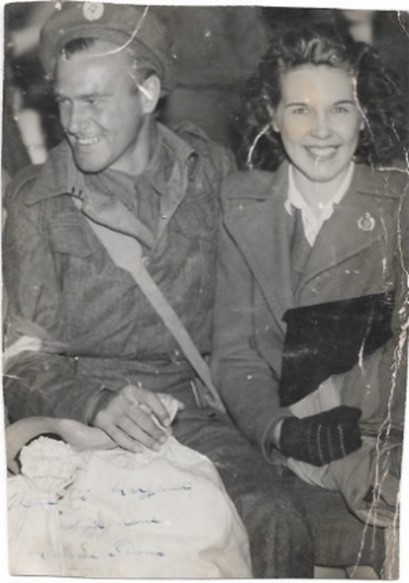 Black and white photograph of Maurice Green and his wife Doris. Maurice is in his uniform they are sat down together, his kitbag across his lap. They are both smiling happy to be reunited.