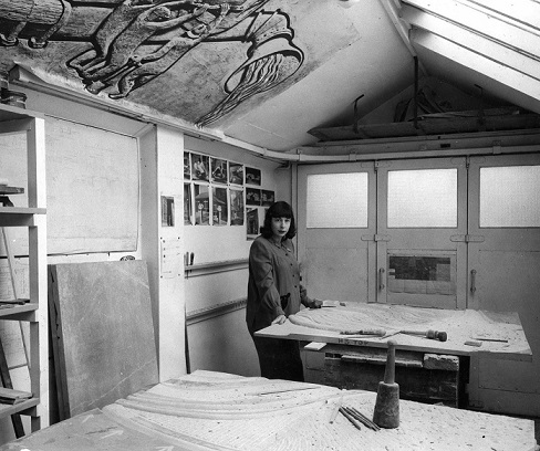 Mitzi in her Manchester garage/studio c.1955 working on the Heaton Moor bas relief. On the wall behind her are photos of the sculpture Quickening (©Estate of the Artist)