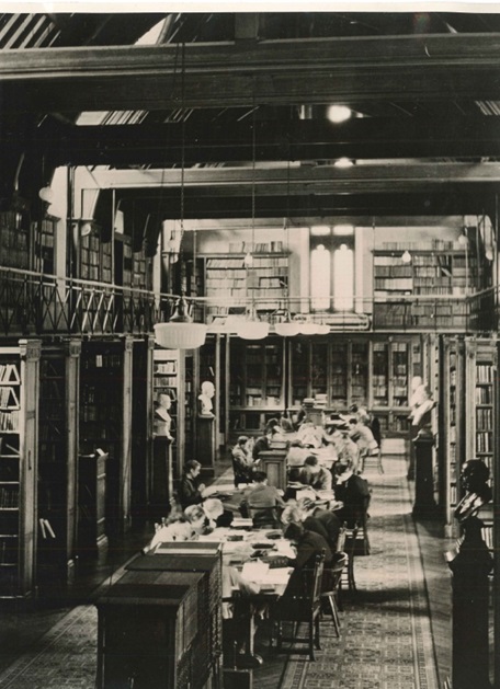 The Tate Library circa 1920 showing students seated in the dimly lit library surrounded by overflowing shelves.
