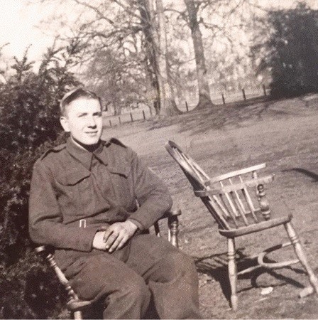 Black and white photograph of William Dickinson Davies sat in profile on a chair, in a garden. He is wearing his uniform, there is a vacant chair next to him.