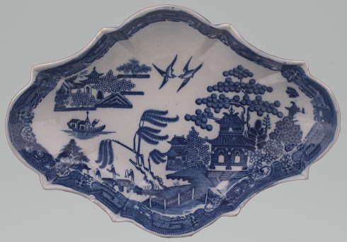 Shallow dish of rhombus shape. It is decorated in the blue and white Willow Pattern in the centre with the design going across the widest plane and a blue border around the edge. 