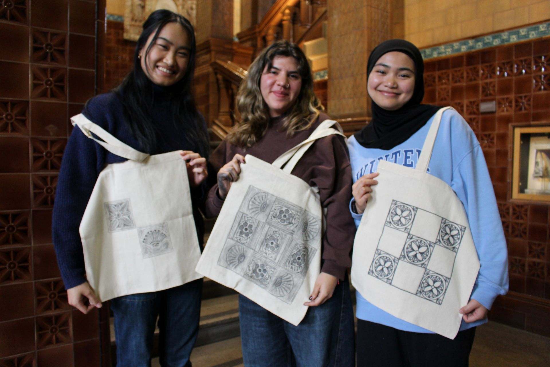 Three female students holding up tote bags with designs on they have created
